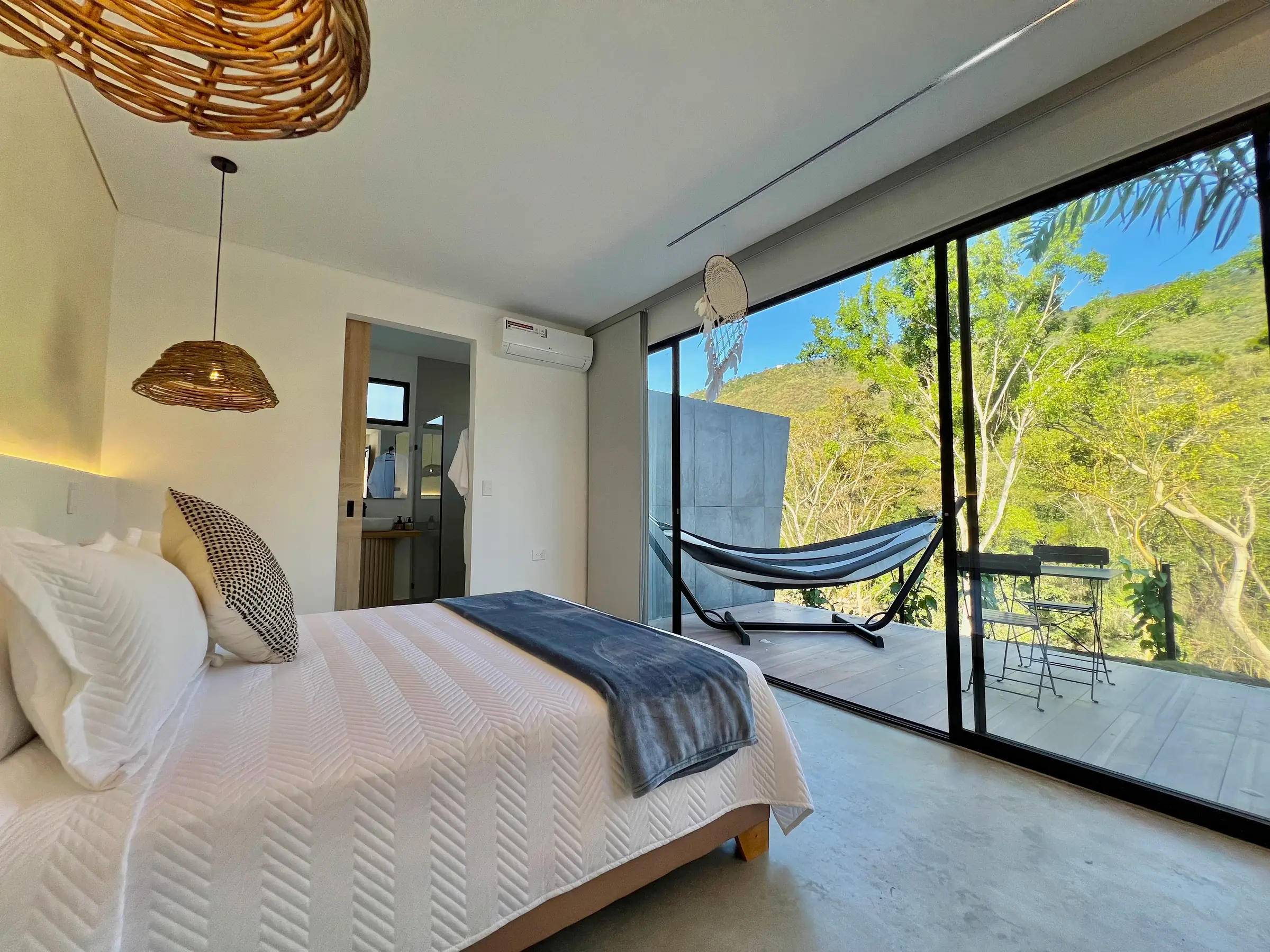 Cama doble grande de la cabaña Deluxe frente al ventanal que se abre a la terraza con hamaca