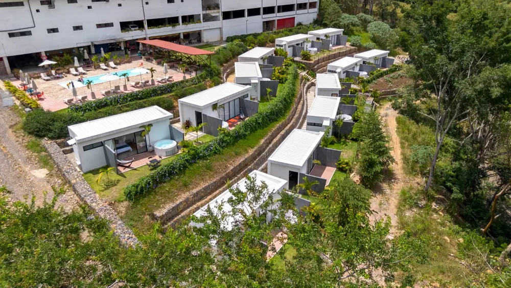 Vista aérea de las cabañas con jacuzzi y jardines, con la piscina de la sede al fondo