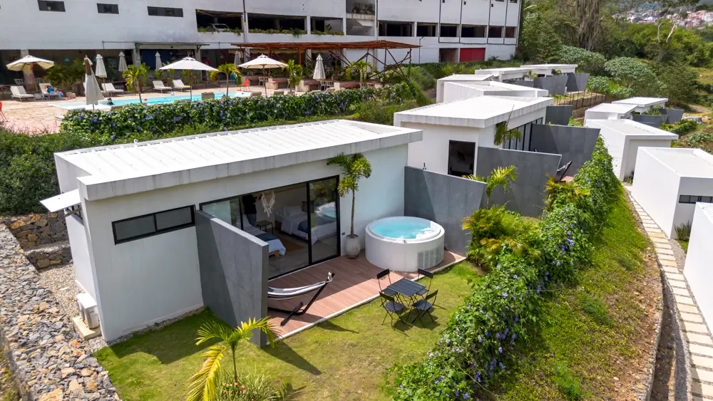 Terraza de una cabaña vista desde el aire: jacuzzi encendido, hamaca, mesa para dos y jardín