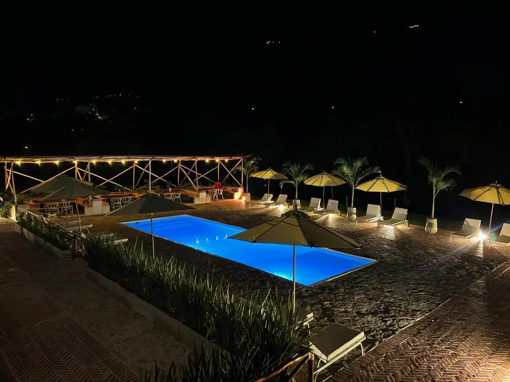 La piscina iluminada de noche, rodeada de sombrillas y luces cálidas