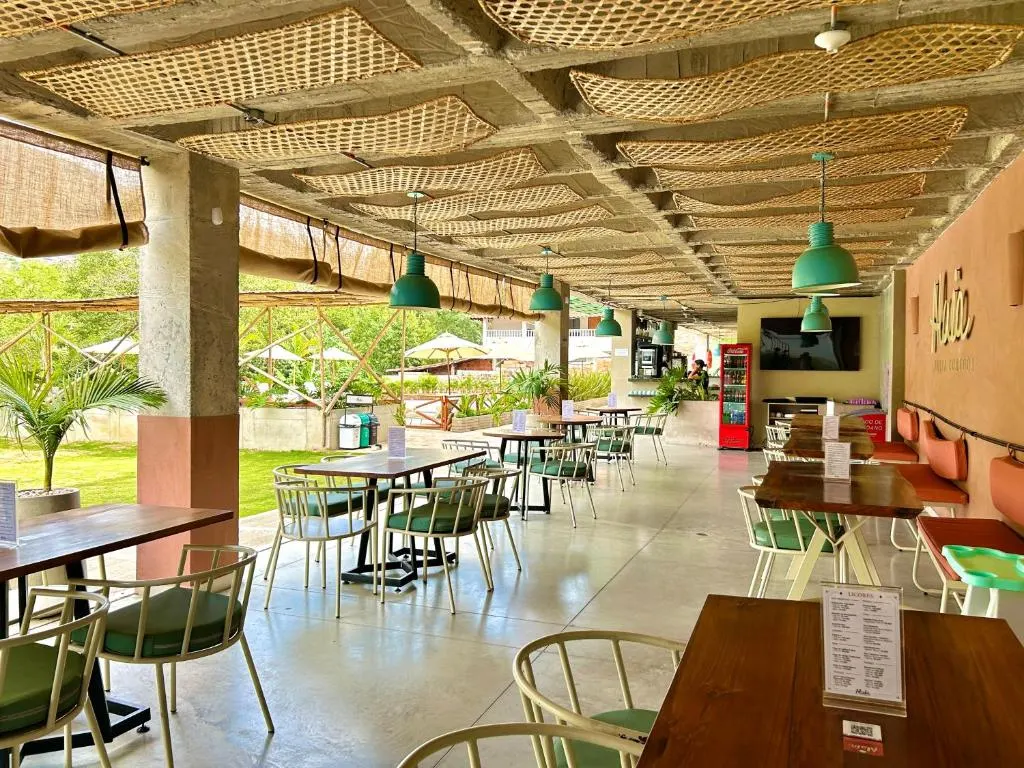 Salón de Alaia Barra Comedor con mesas de madera bajo un techo de esterilla